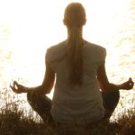 Mujer joven de espaldas sentada en el campo en un atardecer y practicando la meditación Metta Bhavana.