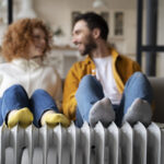 Una pareja joven sentada y reposando sus pies sobre un radiador para disfrutar de la calefacción en casa.