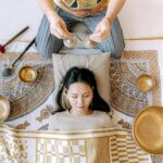 Una mujer tumbada y meditando con sonidos de gongs y diferentes instrumentos meditativos según la sabiduría oriental.