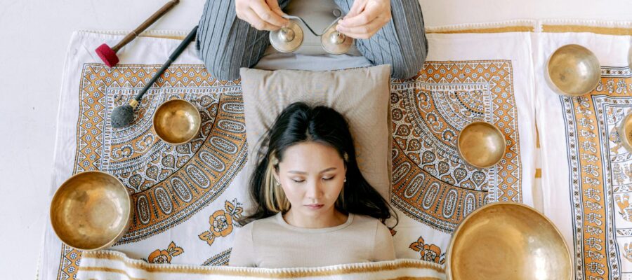 Una mujer tumbada y meditando con sonidos de gongs y diferentes instrumentos meditativos según la sabiduría oriental.